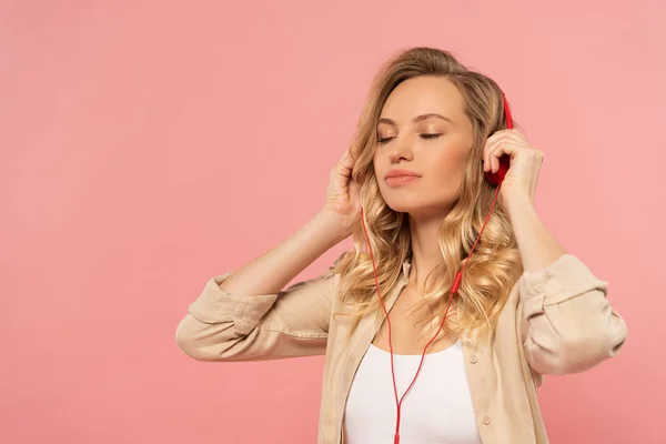 Mujer rubia con los ojos cerrados en auriculares aislados en rosa - foto de stock