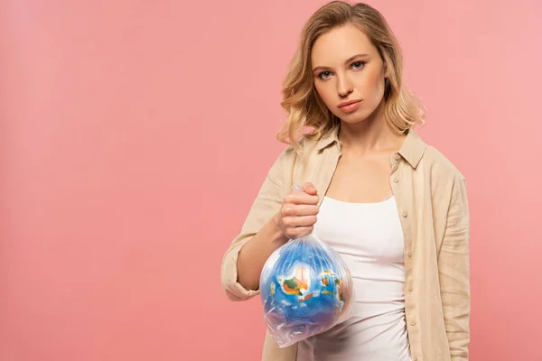 Femme blonde tenant globe dans un paquet de polyéthylène isolé sur rose, concept de réchauffement climatique — Photo de stock