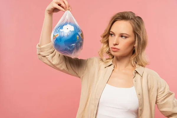 Pensive femme tenant globe dans un paquet de polyéthylène isolé sur rose, concept de réchauffement climatique — Photo de stock
