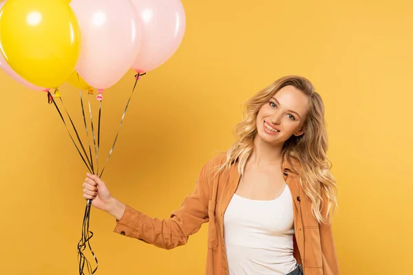 Усміхнена блондинка тримає повітряні кулі ізольовані на жовтому — стокове фото