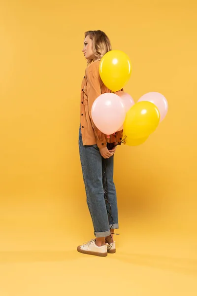 Vue latérale de la femme blonde tenant des ballons sur fond jaune — Photo de stock