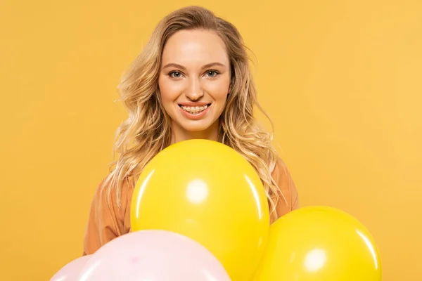 Smiling young woman holding colorful balloons isolated on yellow — Stock Photo