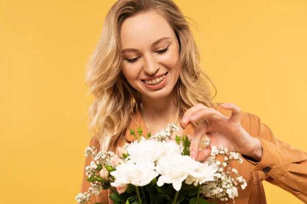 Smiling woman touching flower in bouquet isolated on yellow — Stock Photo