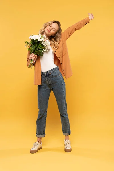 Smiling blonde woman holding bouquet on yellow background — Stock Photo