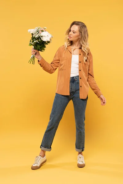 Attractive blonde woman holding bouquet on yellow background — Stock Photo