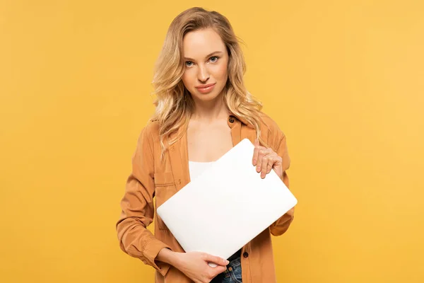 Lächelnde blonde Frau hält Laptop isoliert auf gelb — Stockfoto