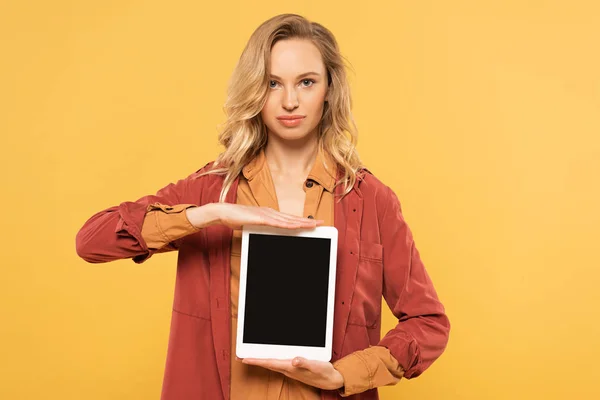 Mujer rubia sosteniendo tableta digital con pantalla en blanco aislada en amarillo - foto de stock