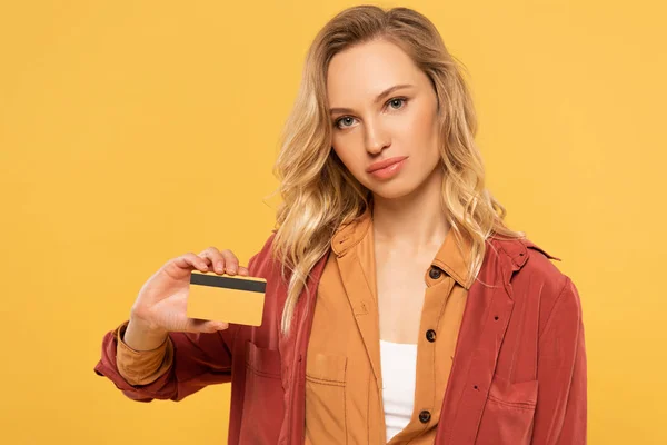 Atractiva mujer rubia sosteniendo tarjeta de crédito aislada en amarillo - foto de stock