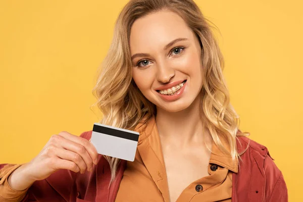 Mujer sonriente sosteniendo tarjeta de crédito aislada en amarillo - foto de stock