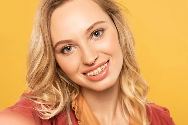 Punto de vista de la cámara de la mujer sonriente con frenos dentales tomando selfie aislado en amarillo - foto de stock