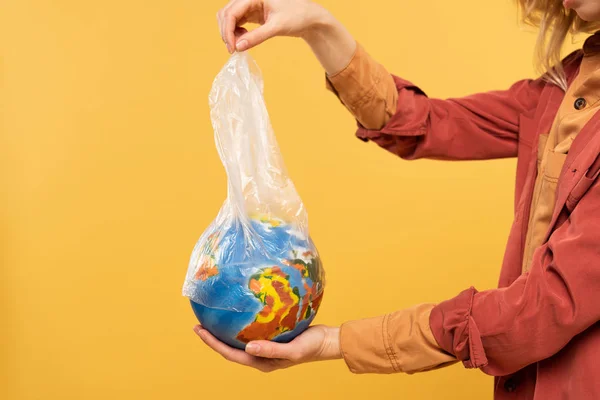 Vue recadrée de la femme tenant le globe et le paquet en plastique isolés sur jaune, concept de réchauffement climatique — Photo de stock