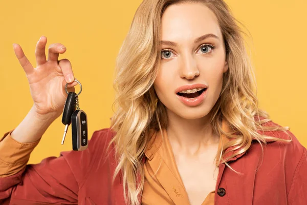 Surprised blonde woman holding car keys isolated on yellow — Stock Photo