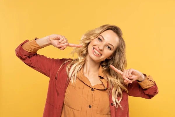 Mulher sorridente com aparelho dentário apontando na boca isolada em amarelo — Fotografia de Stock