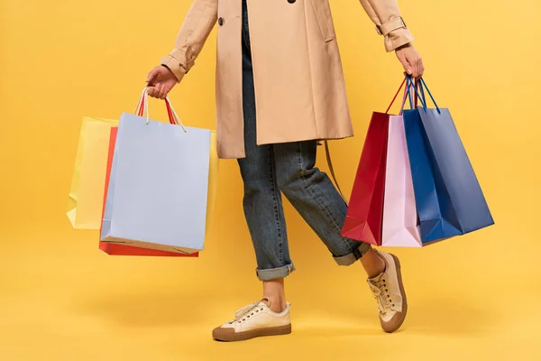 Vista cortada de mulher segurando sacos de compras em mãos no fundo amarelo — Fotografia de Stock