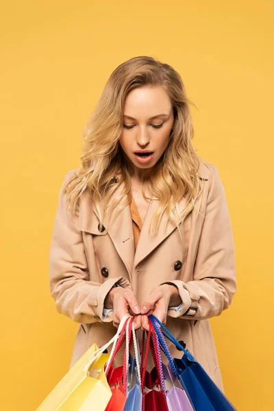 Удивлённая женщина держит сумки, изолированные на желтом — стоковое фото