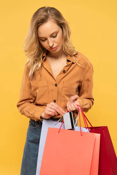 Mujer rubia poniendo tarjeta de crédito en bolsa aislada en amarillo - foto de stock