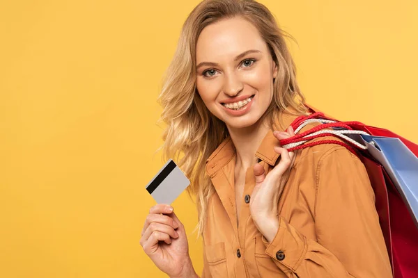Donna sorridente con carta di credito e borse della spesa isolate sul giallo — Foto stock