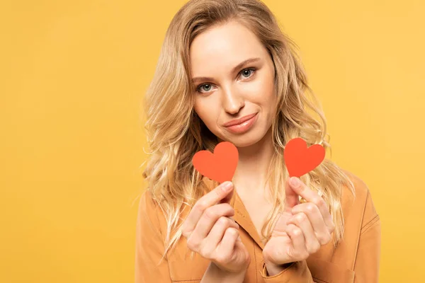 Mujer rubia sonriente sosteniendo corazones de papel aislados en amarillo - foto de stock