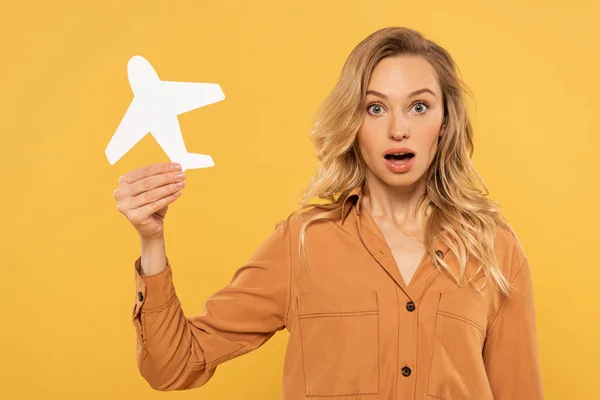 Mulher loira surpreso segurando avião de papel isolado no amarelo — Fotografia de Stock