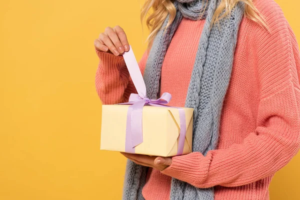 Vista recortada de la mujer desatar cinta en caja de regalo aislado en amarillo - foto de stock