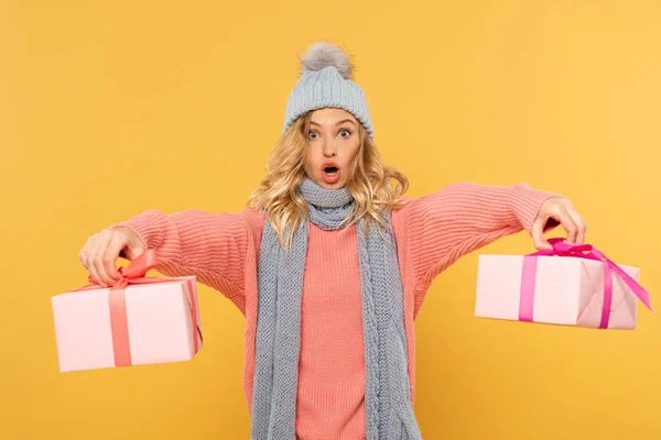 Aufgeregten blonden Frau mit Hut und Schal halten Geschenkboxen isoliert auf gelb — Stockfoto