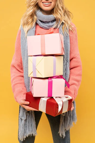 Cropped view of smiling woman in scarf holding gift boxes isolated on yellow — Stock Photo