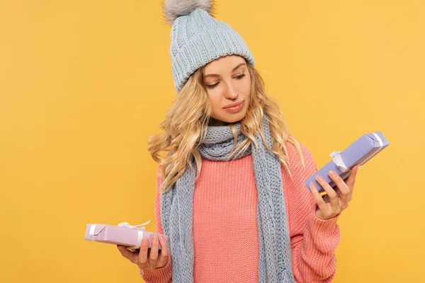 Blonde woman in hat and scarf holding gift boxes isolated on yellow — Stock Photo