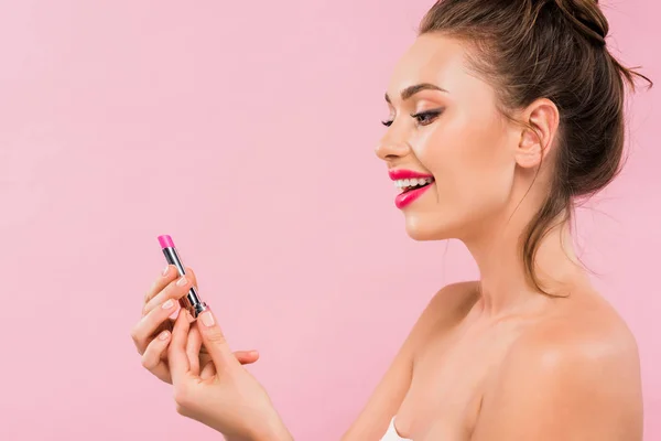 Vista lateral de mujer hermosa desnuda feliz con labios rosados sosteniendo lápiz labial aislado en rosa - foto de stock