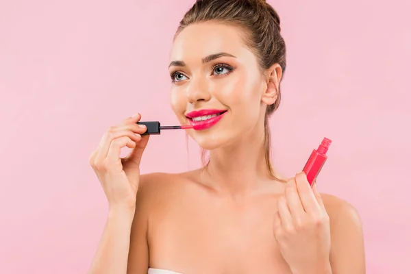 Sonriente mujer hermosa desnuda con labios rosados aplicando brillo labial aislado en rosa - foto de stock