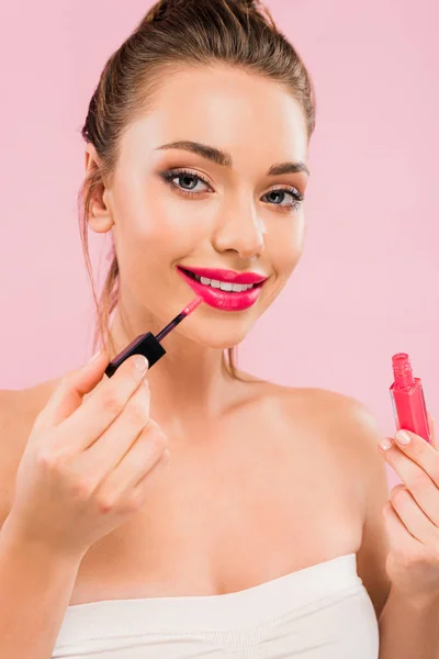 Lächelnde schöne Frau mit rosa Lippen, die Lipgloss isoliert auf rosa aufträgt — Stockfoto