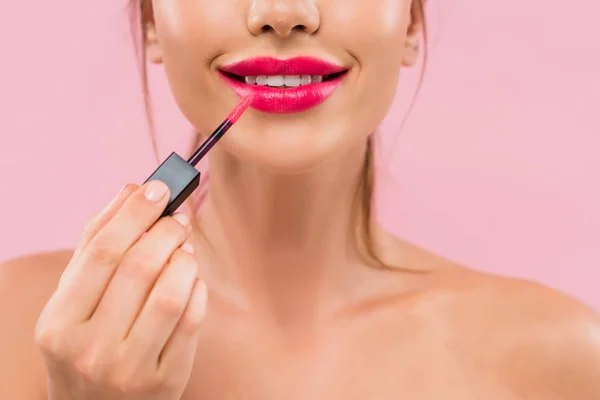 Partial view of smiling naked beautiful woman with pink lips applying lip gloss isolated on pink — Stock Photo