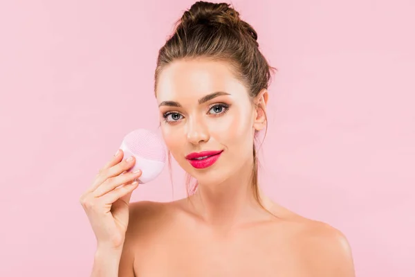 Гола красива жінка з рожевими губами тримає щітку для очищення обличчя ізольована на рожевому — стокове фото