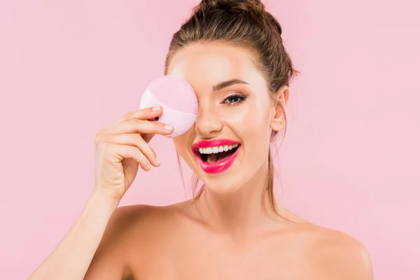 Щаслива гола красива жінка з рожевими губами, що тримає щітку для очищення обличчя ізольована на рожевому — стокове фото
