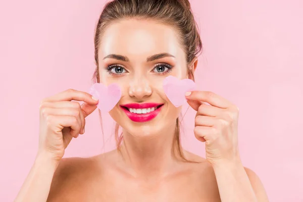 Happy naked beautiful woman with pink lips holding facial heart shaped patches isolated on pink — Stock Photo