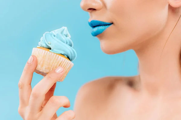 Partial view of naked beautiful woman with blue lips holding cupcake isolated on blue — Stock Photo