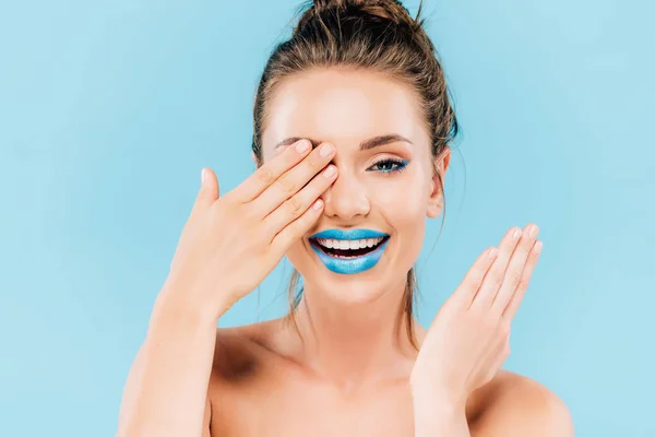 Heureuse belle femme avec lèvres bleues couvrant oeil avec main isolé sur bleu — Photo de stock