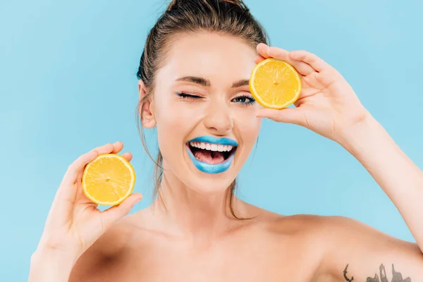 Felice strizzatina d'occhio nuda bella donna con labbra blu che tengono le metà arancioni isolate sul blu — Foto stock