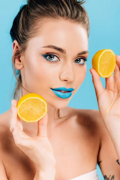 Гола красива жінка з блакитними губами тримає помаранчеві половинки ізольовані на синьому — стокове фото