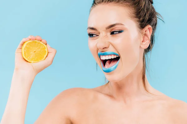 Angry naked beautiful woman with blue lips holding orange half isolated on blue — Stock Photo