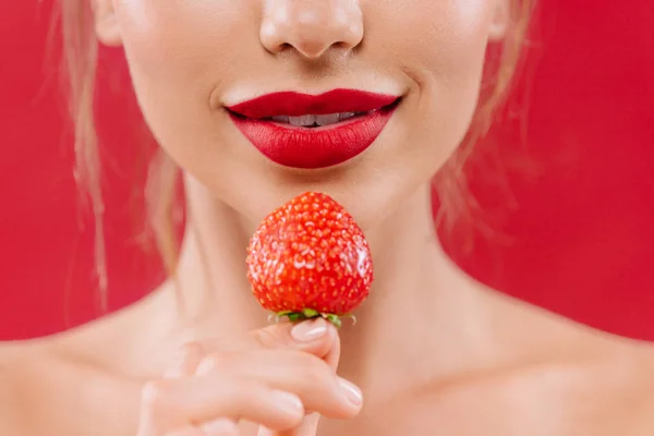 Vista parcial de hermosa mujer desnuda con labios rojos sosteniendo fresa aislada en rojo - foto de stock