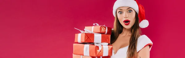 Impactado sexy hermosa chica santa sosteniendo cajas de regalo aisladas en Borgoña, tiro panorámico — Stock Photo