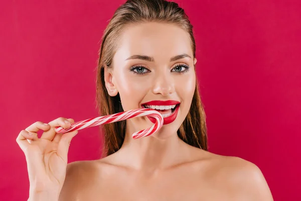 Naked beautiful woman with red lips eating sweet striped candy isolated on burgundy — Stock Photo