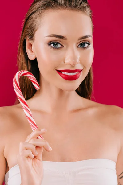 Smiling beautiful woman with red lips holding sweet striped candy isolated on burgundy — Stock Photo