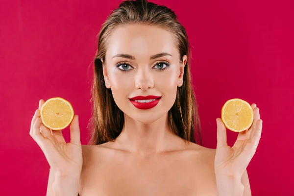 Sourire nu belle femme aux lèvres rouges tenant des moitiés orange isolé sur bordeaux — Photo de stock