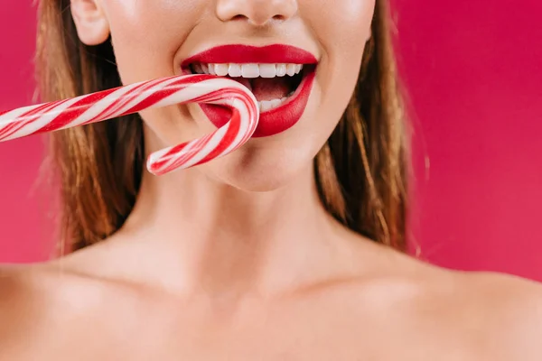 Cropped view of naked beautiful woman with red lips biting sweet striped candy isolated on burgundy — Stock Photo