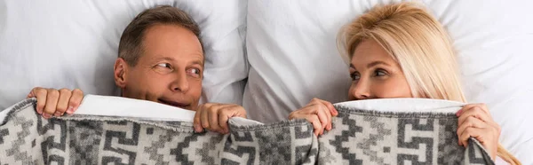 Panoramic shot of mature couple covering with blanket and looking at each other — Stock Photo