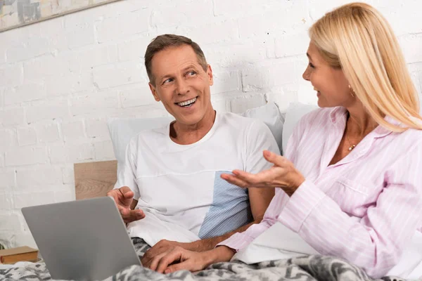Lächelndes Paar schaut einander an, während es Laptop im Bett benutzt — Stockfoto