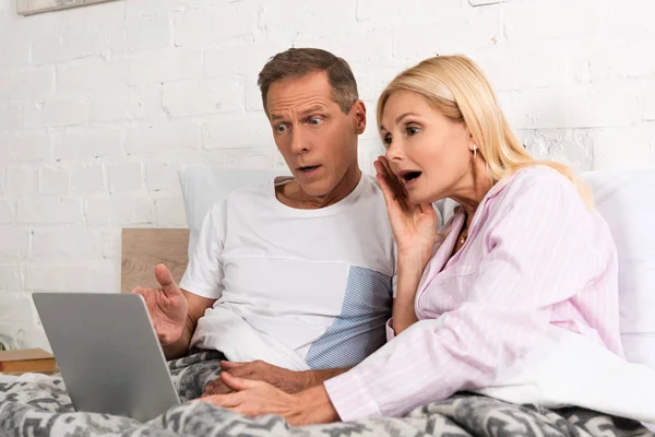 Casal chocado olhando para laptop juntos na cama — Fotografia de Stock