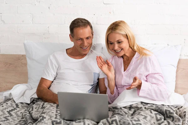 Sorrindo casal olhando para laptop juntos na cama — Fotografia de Stock