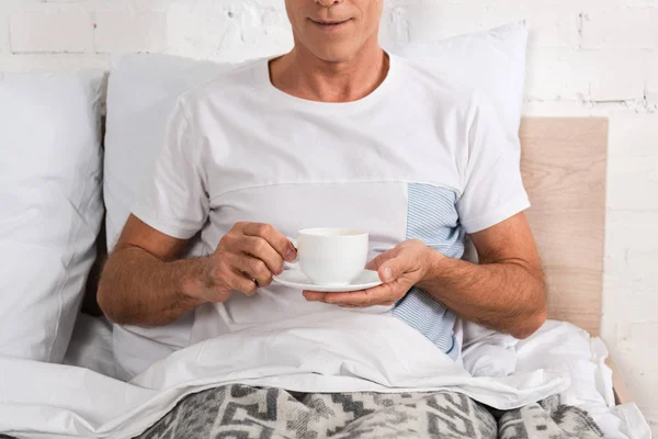 Vista ritagliata dell'uomo che tiene la tazza di caffè a letto — Foto stock